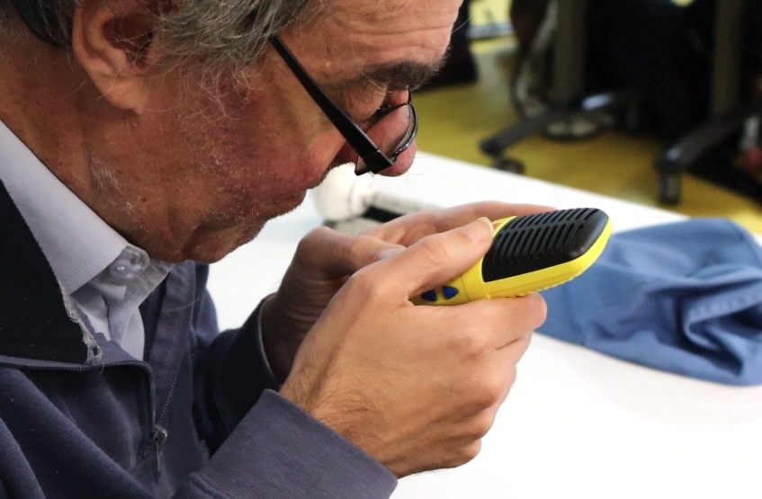 A man wearing glasses and a blue top is holding a bright yellow recording device close to his face and is pressing the buttons.